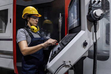 Ingenieur mit Schutzhelm bei der Bedienung einer CNC-Maschine in einer modernen Fabrik - AAZF00635