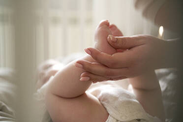 Mother holding feet of baby girl lying on bed - ABIF01991