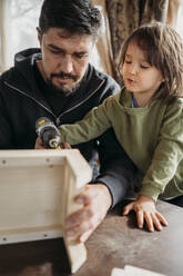 Son learning to build up birdhouse with father at home - ANAF01437