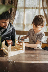 Son learning to build up birdhouse with father at home - ANAF01445
