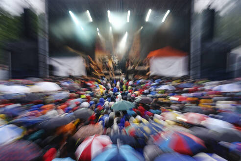 Überfülltes Musikfestival mit Fans, die Regenschirme tragen - MAMF02857