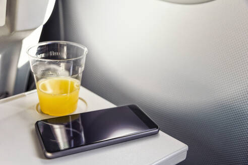 Smart Phone und Glas Orangensaft im Flugzeug - MAMF02863