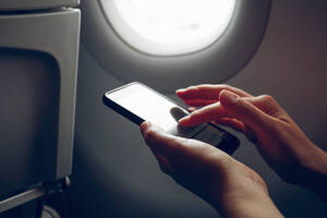 Hands of woman surfing net through smart phone in airplane - MAMF02864
