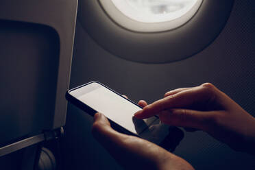 Frau scrollt im Flugzeug auf ihrem Smartphone - MAMF02865