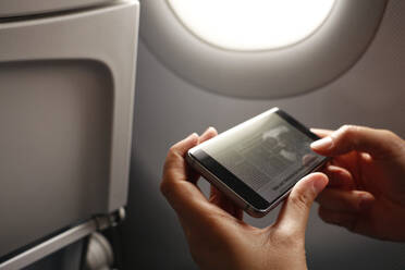 Hände einer Frau, die ein Smartphone mit einem Nachrichtenartikel auf dem Display eines Flugzeugs hält - MAMF02866