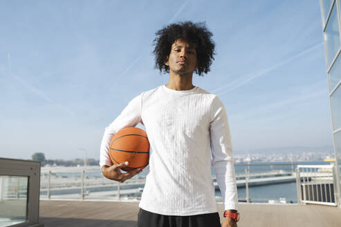 Selbstbewusster junger Sportler hält Basketball an einem sonnigen Tag - ALKF00287