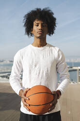 Athlete with curly hair holding basketball at sunny day - ALKF00289