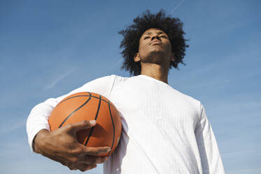 Sportler hält Basketball unter dem Arm mit Himmel im Hintergrund - ALKF00294