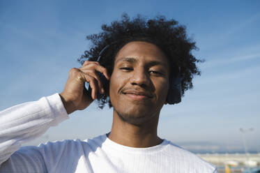 Smiling athlete holding wireless headphones at sunny day - ALKF00299