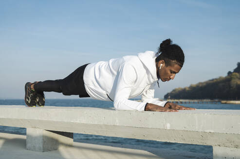 Sportler beim Üben der Plank-Position am Geländer an einem sonnigen Tag - ALKF00307