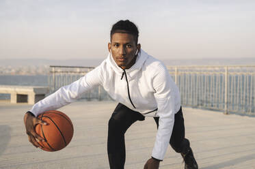 Selbstbewusster Sportler dribbelt mit Basketball auf dem Steg - ALKF00312