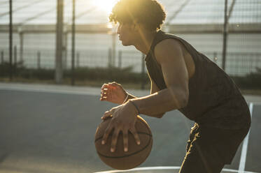 Sportler dribbelt Basketball auf einem Sportplatz bei Sonnenuntergang - ALKF00325