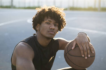 Athlete with curly hair holding basketball at court - ALKF00328