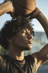 Athlete holding basketball overhead at sunset - ALKF00330