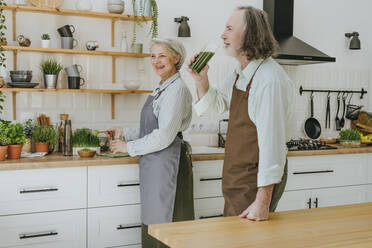 Man drinking wheatgrass jucie standing with woman in kitchen at home - YTF00859