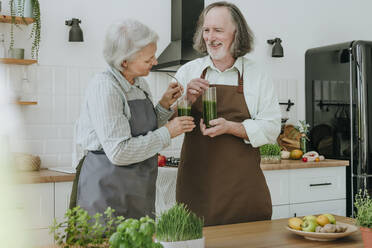 Smiling man having detox juice with woman in kitchen at home - YTF00864