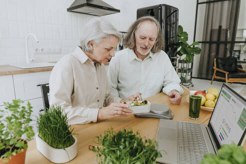 Frau und Mann wiegen Brotdose auf einer Waage in der Küche zu Hause - YTF00875