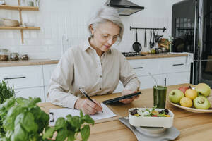 Frau bei der Menüplanung mit Tablet-PC in der Küche zu Hause - YTF00879