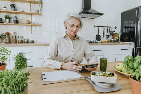 Mature woman with tablet PC in kitchen at home - YTF00880