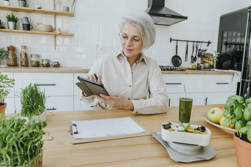 Mature woman using tablet PC at table in home - YTF00881