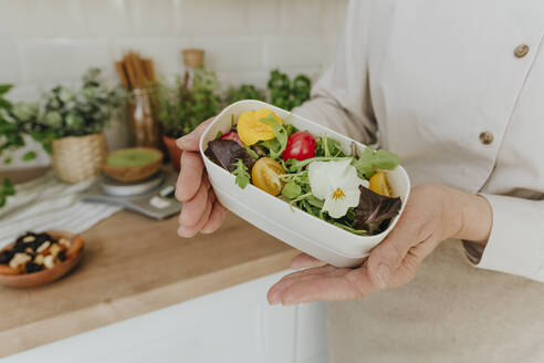 Hands of woman holding healthy salad bowl in kitchen at home - YTF00885