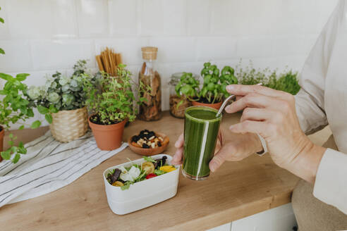 Woman holding glass of detox juice with salad on counter in kitchen at home - YTF00887