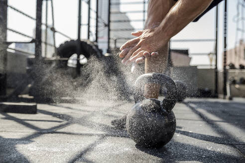 Mann staubt Sportkreide ab und trainiert mit einer Kettlebell auf dem Dach eines Fitnessstudios - IKF00695