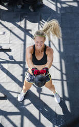 Frau trainiert mit Kettlebell auf dem Dach eines Fitnessstudios - IKF00698