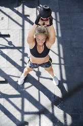 Frau trainiert mit Kettlebell im Fitnessstudio auf der Terrasse - IKF00699