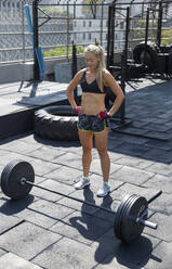 Woman standing in front of barbell weights at rooftop gym - IKF00707