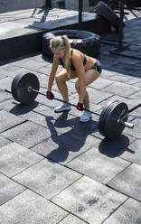 Frau hebt Langhantelgewichte in einem Fitnessstudio auf dem Dach an einem sonnigen Tag - IKF00708