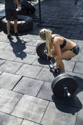 Woman lifting weights at outdoor gym on sunny day - IKF00712