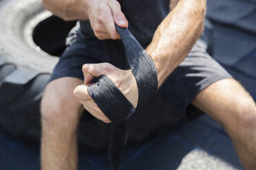 Man wrapping strap on hand at rooftop gym - IKF00715