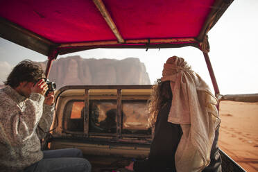 Man photographing woman through camera in car on a desert trip - PCLF00543