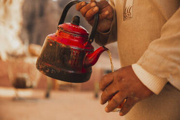 Mann mit Teekanne gießt Tee in Tasse - PCLF00551