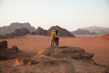 Loving couple standing on rock at sunset in desert - PCLF00567