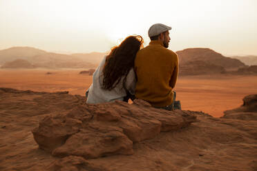 Couple sitting together on rock looking at desert at sunset - PCLF00576