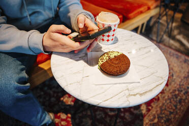 Junge fotografiert Kuchen mit seinem Smartphone in einem Cafe - NLAF00030