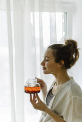 Woman smelling freshly brewed tea at home - IEF00416