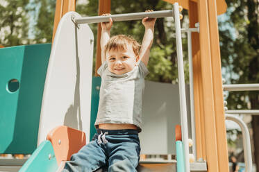 Boy hanging on slide in playground - ANAF01459