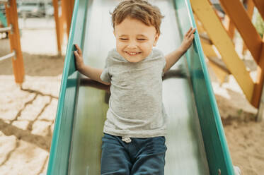 Fröhlicher Junge hat Spaß auf der Rutsche auf dem Spielplatz - ANAF01461