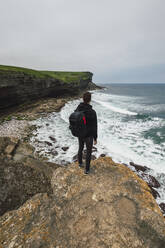 Junger Mann steht auf einem Felsen am Strand - RSGF00911
