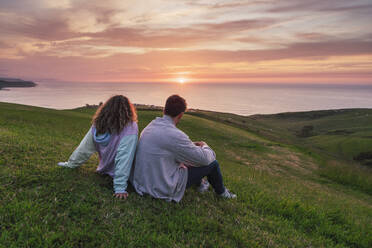Friends looking at sunset sitting on grass - RSGF00913