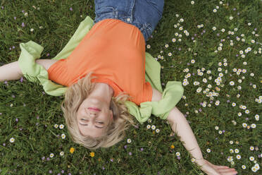 Smiling woman with eyes closed lying amidst flowers on grass - OSF01582