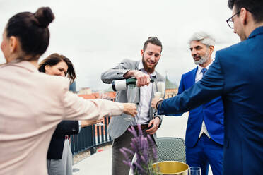 Eine große Gruppe fröhlicher Geschäftsleute, die auf einer Dachterrasse in der Stadt eine Party feiern und Champagner ausschenken. - HPIF18528