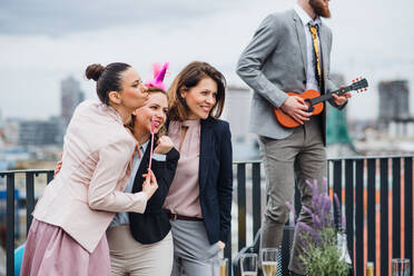 Eine große Gruppe fröhlicher Geschäftsleute, die auf einer Dachterrasse in der Stadt eine Party feiern und für ein Foto posieren. - HPIF18533