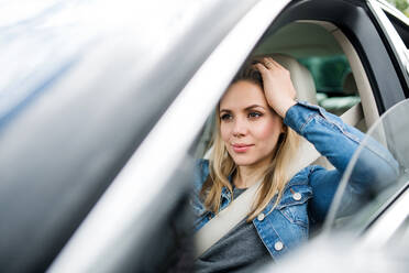 Eine gelangweilte junge Fahrerin sitzt im Auto und wartet. - HPIF18549