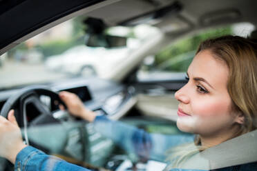 Eine junge Fahrerin sitzt in einem Auto und wird durch eine Glasscheibe fotografiert. - HPIF18550