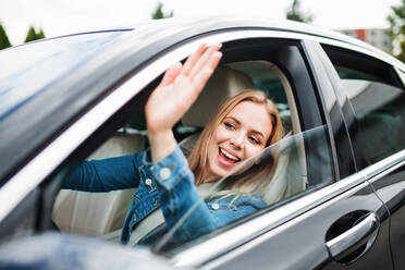 Eine junge Fahrerin sitzt im Auto und begrüßt jemanden. - HPIF18552