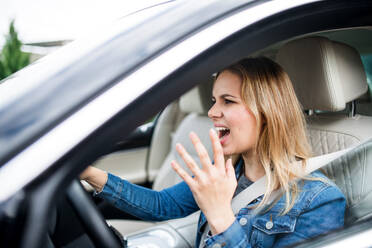 Wütende junge Fahrerin sitzt im Auto und schreit während der Fahrt. - HPIF18554